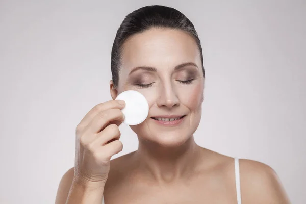ミセル水綿パッドを使用する灰色の背景上の顔から化粧を削除する熟女 — ストック写真