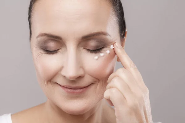 Middle Aged Woman Applying Cream Skin Eyes Grey Background — Stock Photo, Image