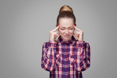 kafasını gri arka plan üzerinde acıyla dokunmadan toplanan topuz saç modeli ile kareli gömlekli sarışın kadın