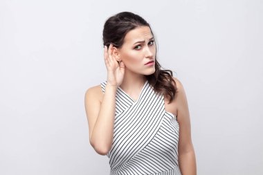Makyaj ve ayakta, kulak yakınındaki elini tutarak, kameraya bakıyor ve gri arka plan üzerinde dinliyoruz çizgili elbise ile ciddi güzel genç esmer kadın portresi.