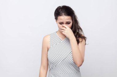 Üzgün depresif güzel genç esmer kadınla makyaj ve çizgili elbise ayakta portresi, kafa tutarak ve crying on arka plan gri.