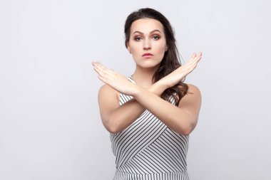 Ciddi güzel genç esmer kadın makyaj ile ve çapraz eller ve gri arka plan üzerinde uyarı yanlış yolu ile çizgili elbise ayakta portre.