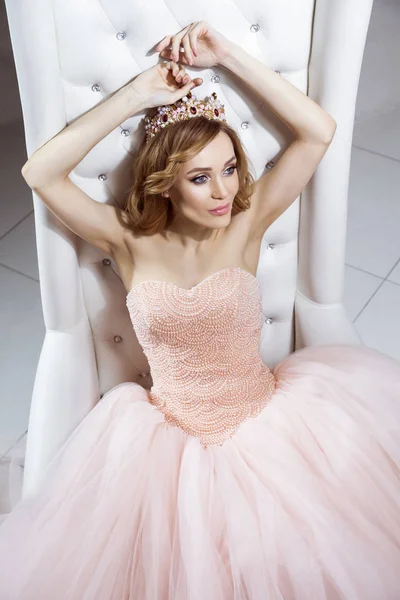 Bela Mulher Coroa Vestido Rosa Luxuoso Sentado Poltrona Branca Elegante — Fotografia de Stock
