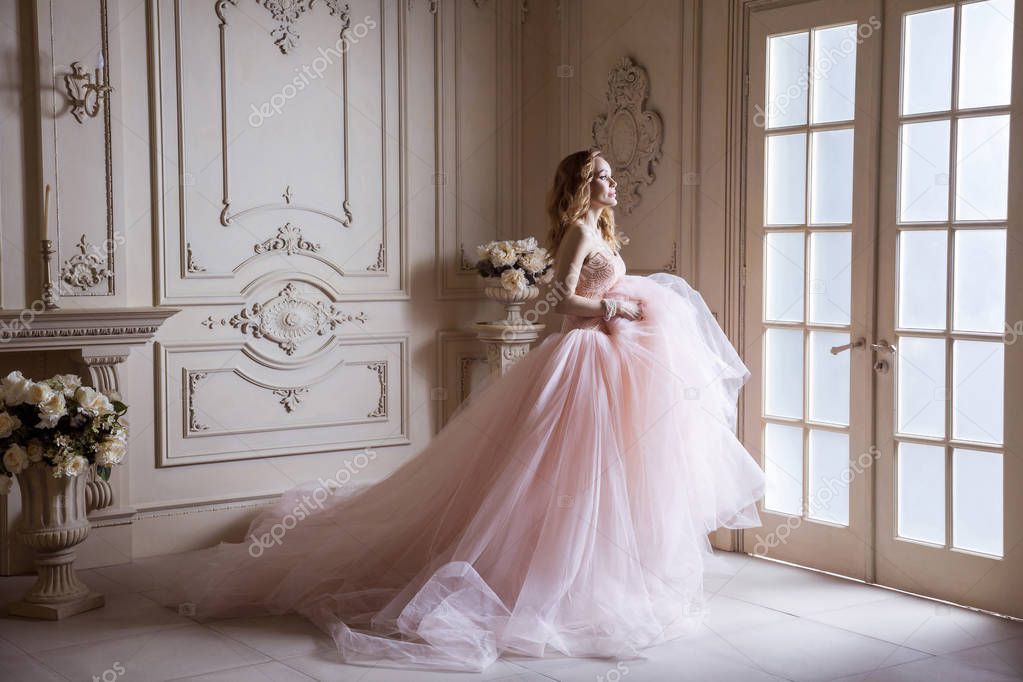 beautiful woman in crown and luxurious pink dress posing in vintage room interior 