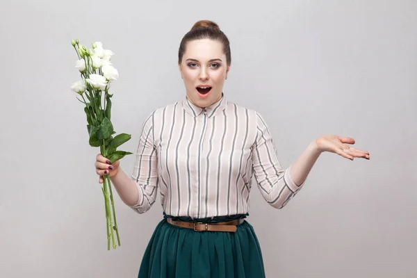 ストライプのシャツ 緑のスカートが灰色の背景に上げられた腕と白い花のブーケを持って驚くロマンチックな若い女性の肖像画 — ストック写真