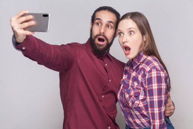 Mobil smartphone vasıl bakarak şok çift portre kocaman gözleriyle görüntülemek ve gri arka plan üzerine ağzı açık 