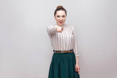 Çizgili gömlekli ve makyaj ve toplanan yasağı saç modeli ayakta ve kameraya gösteren yeşil etek hayran güzel genç kadın portresi 