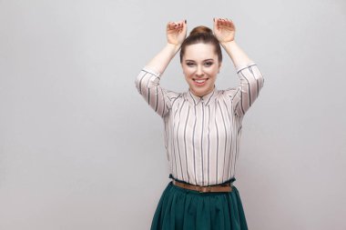 Çizgili gömlekli ve kameraya bakarak ve bunny jest gösterilen toplanan yasağı saç modeli ile yeşil etek komik güzel ve genç birbayan