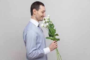 Büyüleyici zevk romantik genç adam beyaz buket tutarak ve kokulu mavi gömlekli yan görünüm 