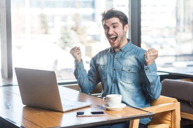 Portre hayran memnun sakallı genç freelancer kafede oturan ve dişlek gülümseme ile laptop bakarken zafer kot gömlek 
