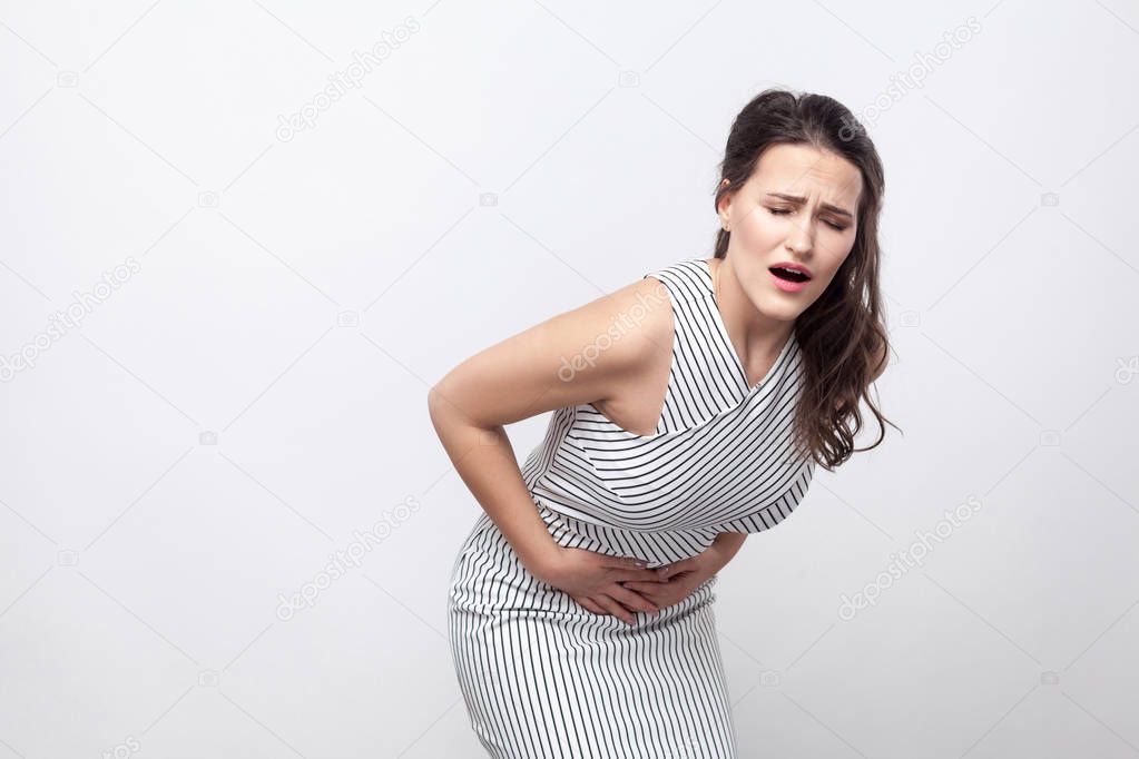 sick unhappy  brunette woman in striped dress bending in half from pain in belly, stomach pain concept 