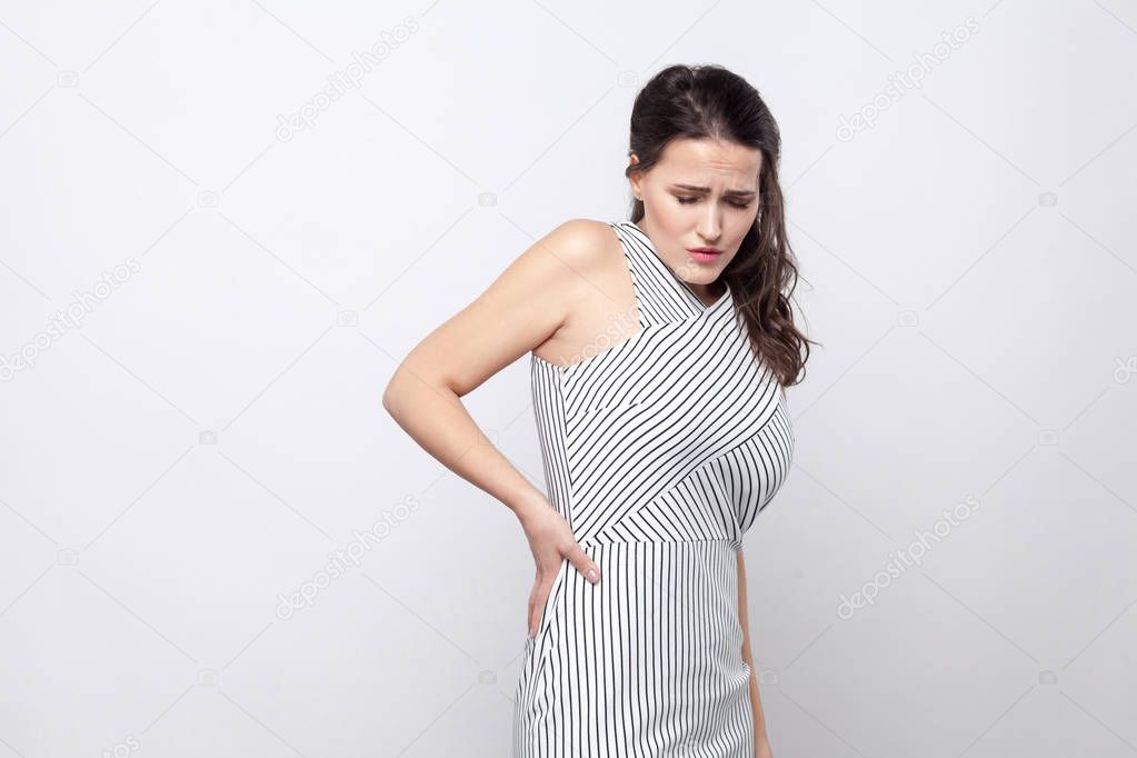  unhappy beautiful  brunette woman in striped dress having kidney pain and pressing hand to flank to relieve pain with helpless face