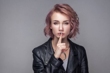 Kısa pembe saç ve makyaj dudaklarında parmak ile siyah deri ceket ayakta sessiz işaret gösteren süre ile ciddi güzel kadın portresi 