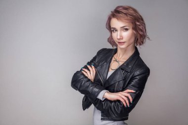 Kısa pembe saç ve makyaj ile çapraz eller ayakta ve kameraya bakarak siyah deri ceketli ile memnun mutlu kadın portresi 