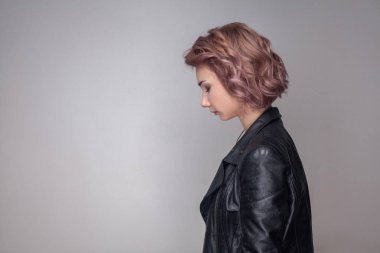 side view of sad depressed beautiful woman with short pink hairstyle and makeup in black leather jacket standing with closed eyes  on grey background. clipart
