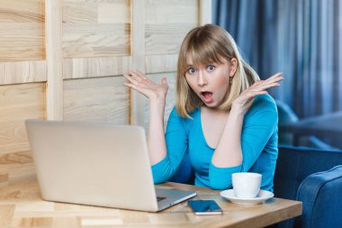 sürpriz büyük gözleri ve yükseltilmiş silah kafede otururken laptop haber okuma ile mavi bluz içinde duygusal şok genç iş kadını   