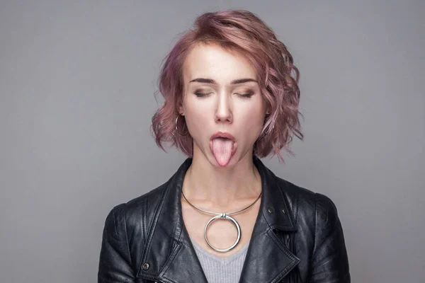 短いピンクの髪型と目を閉じて立っていると舌出しを示す黒い革のジャケットで化粧の面白い女性の肖像画 — ストック写真