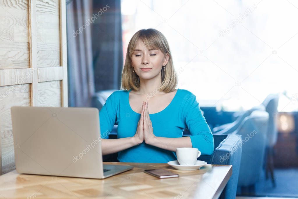 successful attractive woman freelancer in blue blouse holding hands like have meditative to have emotional pleasure while sitting in cafe  
