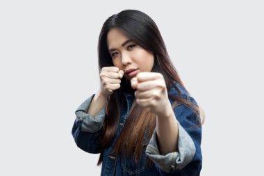 ciddi güzel esmer Asyalı genç kadını boks yumruk ile ayakta ve kameraya ışık gri arka plan üzerinde seyir sıradan mavi Kot ceket