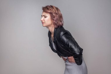 kadın ayakta ve tutarak onun hasta karın, mide ağrısı kavramı rahat tarzı siyah deri ceketli kısa pembe saç modeli ile yan görünüm 