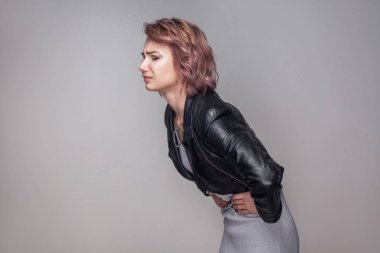side view of woman with short pink hairstyle in casual style black leather jacket standing and holding her sick belly, Stomach pain concept  clipart