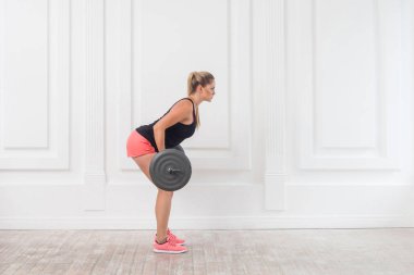 genç atletik güzel vücut geliştirmeci kadın pembe şort ve halter ile ağız kavgası yapıyor ve gluteus kas spor salonunda egzersiz siyah top yan görünüm 