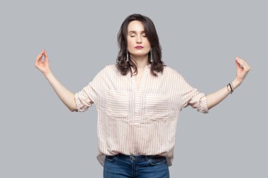 makyaj ve ayakta ve yoga poz gri arka plan üzerinde meditasyon kıvırcık saç modeli ile rahat çizgili turuncu gömlekli çekici esmer kadın sakin. 
