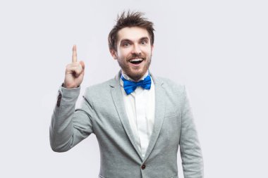 yakışıklı heyecanlı sakallı adam rahat gri renk takımlı ve mavi ayakta ve kameraya dişlek gülümseme ile ışık gri arka plan üzerinde seyir papyon.