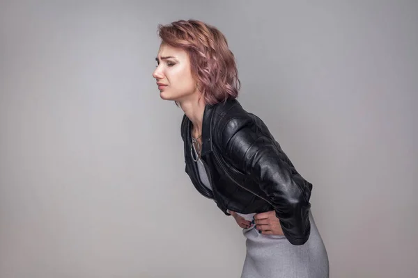 カジュアルなスタイルのブラック レザー ジャケット立て 彼女の病気の腹 胃の痛みの概念を保持短いピンクの髪型の女性の側面図 — ストック写真