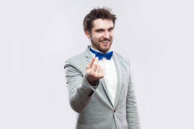 Sıradan gri renk takımlı ve mavi para hareketi el ile ayakta ve kameraya kurnaz yüzü ile ışık gri arka plan üzerinde seyir papyon komik sakallı yakışıklı portresi