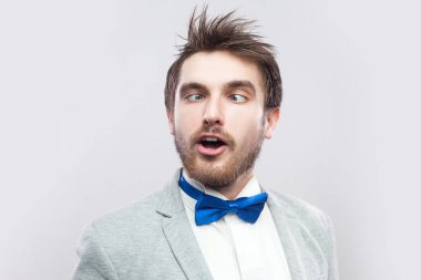 çılgın komik yakışıklı sakallı adam rahat gri renk takımlı ve mavi çapraz gözlerle ayakta ve açık gri renkli Burnuna bakarak papyon.