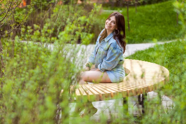 캐주얼 스타일 벤치에 앉아서 공원에서 미소로 카메라를 여자의 — 스톡 사진