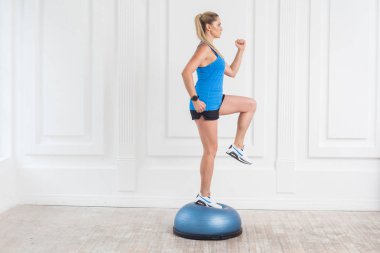 Spor salonunda çalışırken Dizimin üstüne bosu denge sportif sarışın kadın siyah şort ve mavi top yan görünüm kaldırdı 