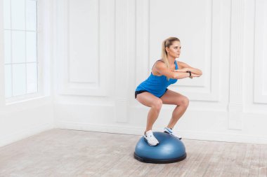 Sportif sarışın kadın siyah şort ve mavi en iyi denge bosu denge eğitmen üzerinde tutarak ağız kavgası yaparken spor salonunda çalışma