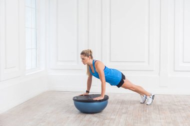 Sportif güzel genç atletik sarışın kadın siyah şort ve mavi en iyi spor salonunda bosu denge eğitmen olarak karın kasları için tahta yaparken çalışma odaklı 