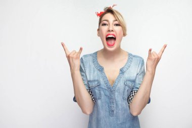 güzel genç kadın rahat mavi kot gömlek ve beyaz arka plan üzerinde izole çığlık makyaj ve kırmızı kafa bandı duran kaya işaretleri ile şaşırttı.
