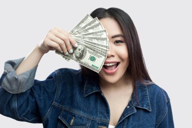 Nakit dolar tutan ve kat yarı-in yüz gri arka plan üzerinde dişlek gülümseme ile mavi kot ceketli güzel mutlu genç Asyalı kadın portresi