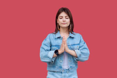 Portre sakin güzel esmer genç kadının palm el ile ayakta ve yoga poz kırmızı zemin üzerine meditasyon yapıyor kot rahat tarzı makyaj ile.