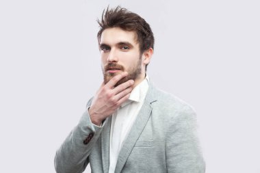 Beyaz gömlek ve rahat gri takım dokunma yüzüne yakışıklı sakallı ciddi adamın portresi ve açık gri arka planda kamera bakıyor.