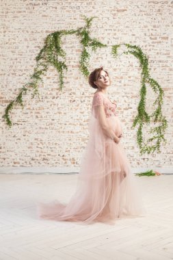 tam uzunlukta portre şehvetli güzel hamile genç kadın pembe elbise ile sevgi göbek ve tuğla duvar arka plan üzerinde poz, gebelik son ay kavramını tutan