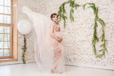 tam uzunlukta portre şehvetli güzel hamile genç kadın pembe elbise ile sevgi göbek ve tuğla duvar arka plan üzerinde poz, gebelik son ay kavramını tutan
