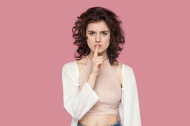 pembe arka planda sessizlik jest göstererek dudaklar üzerinde parmak ile rahat tarzı ayakta kıvırcık saç modeli ile ciddi güzel esmer genç kadın.