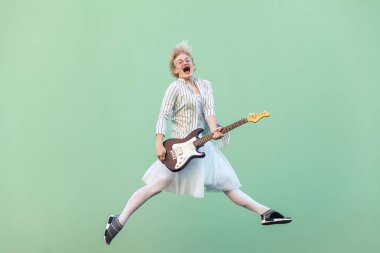 beyaz giysiler ve elektrik gitar çığlık ve açık yeşil arka plan üzerinde atlama gözlüklü çizgili bluz mutlu genç sarışın kadın.