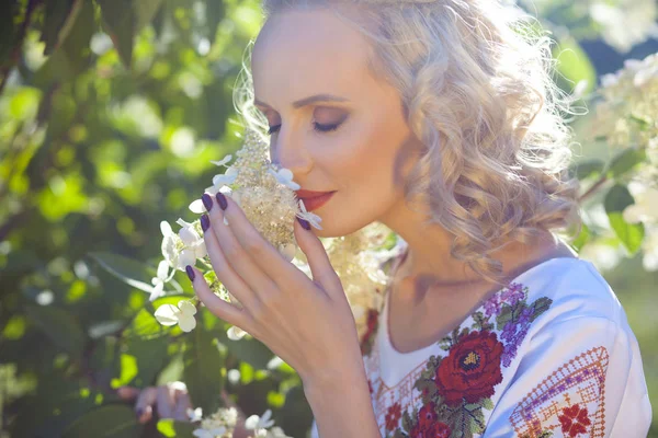 スタイリッシュなウクライナの刺繍と庭に白い花でブッシュの近くにポーズの赤いスカートに身を包んだ魅力的な女性の肖像画 — ストック写真
