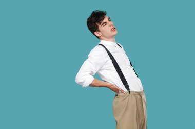 Yakışıklı hipster kıvırcık genç işadamı yan görünümü klasik beyaz gömlek ve askı ayakta ve mavi arka plan onun acı geri tutarak