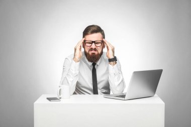 beyaz gömlek ve siyah kravat stresli yüzü ile grimacing duygusal üzgün genç yönetici ve dizüstü bilgisayar ile ofis masasında otururken tapınakyakınında parmakları tutarak 