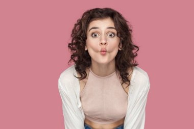 pembe arka planda kamera bakarken büyük gözleri ile ayakta ve balık dudakları gösteren rahat tarzı kıvırcık saç modeli ile komik güzel esmer genç kadın.