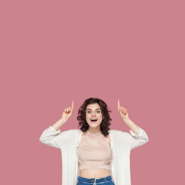 rahat tarzı kıvırcık saç modeli ile heyecanlı güzel esmer genç kadın işaret ve pembe arka plan üzerinde şaşkın yüzü ile kamera bakıyor