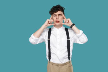 üzgün yakışıklı hipster kıvırcık genç işadamı klasik beyaz gömlek ve askı da başını tutarak mavi arka planda baş ağrısı hissederken