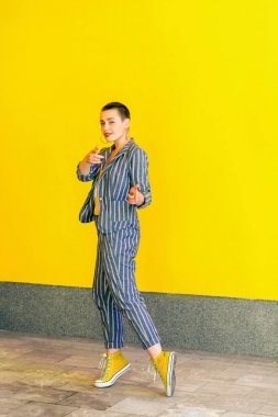 mutlu dişli gülen genç kısa saç güzel hipster kadın sarı gömlek ve çizgili takım elbise görünümlü ve sarı arka plan üzerinde kamera işaret.